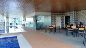A spacious indoor area with a pool, dining tables, and chairs.