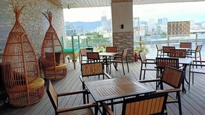 An outdoor seating area with wicker chairs and tables, a brick wall, and a view of the cityscape.