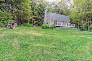 A house with a sloped roof, a porch, and a forested backdrop.