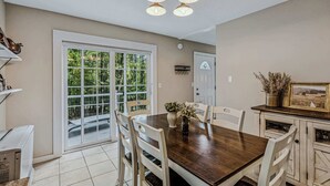 A dining area with a wooden table, white chairs, a ceiling light fixture, a door, and a view of greenery outside. - House on Private Acres with Fire Pit, Quechee (Quechee)