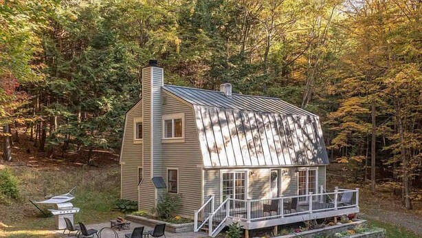 A two-story wooden house with a metal roof, a porch with white railings, and a small deck area. - House on Private Acres with Fire Pit, Quechee (Quechee)