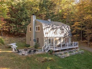 A two-story wooden house with a metal roof, a porch with white railings, and a small deck area.