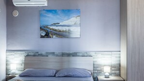 A bedroom with a bed, pillows, a bedside lamp, a wall-mounted air conditioner, and a painting of a coastal scene. - Holiday Home 'Abbacari 1' with Sea View, Wi-Fi and Air Conditioning (Realmonte)