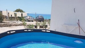 A rectangular outdoor swimming pool with a blue tiled interior, surrounded by a wicker fence, and a view of the sea in the background. - Holiday Home 'Abbacari 1' with Sea View, Wi-Fi and Air Conditioning (Realmonte)