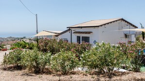 A white building with a tiled roof, surrounded by flowering plants and a clear sky. - Holiday Home 'Abbacari 1' with Sea View, Wi-Fi and Air Conditioning (Realmonte)