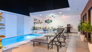 Un área de piscina moderna al aire libre con sillones, una zona de estar y un ventilador de techo.