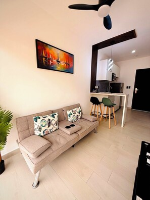 A modern living room with a sofa, a dining area with chairs, a kitchen in the background, and a ceiling fan. - Ocean Dream Apartments E1-A1 (San Juan del Sur)