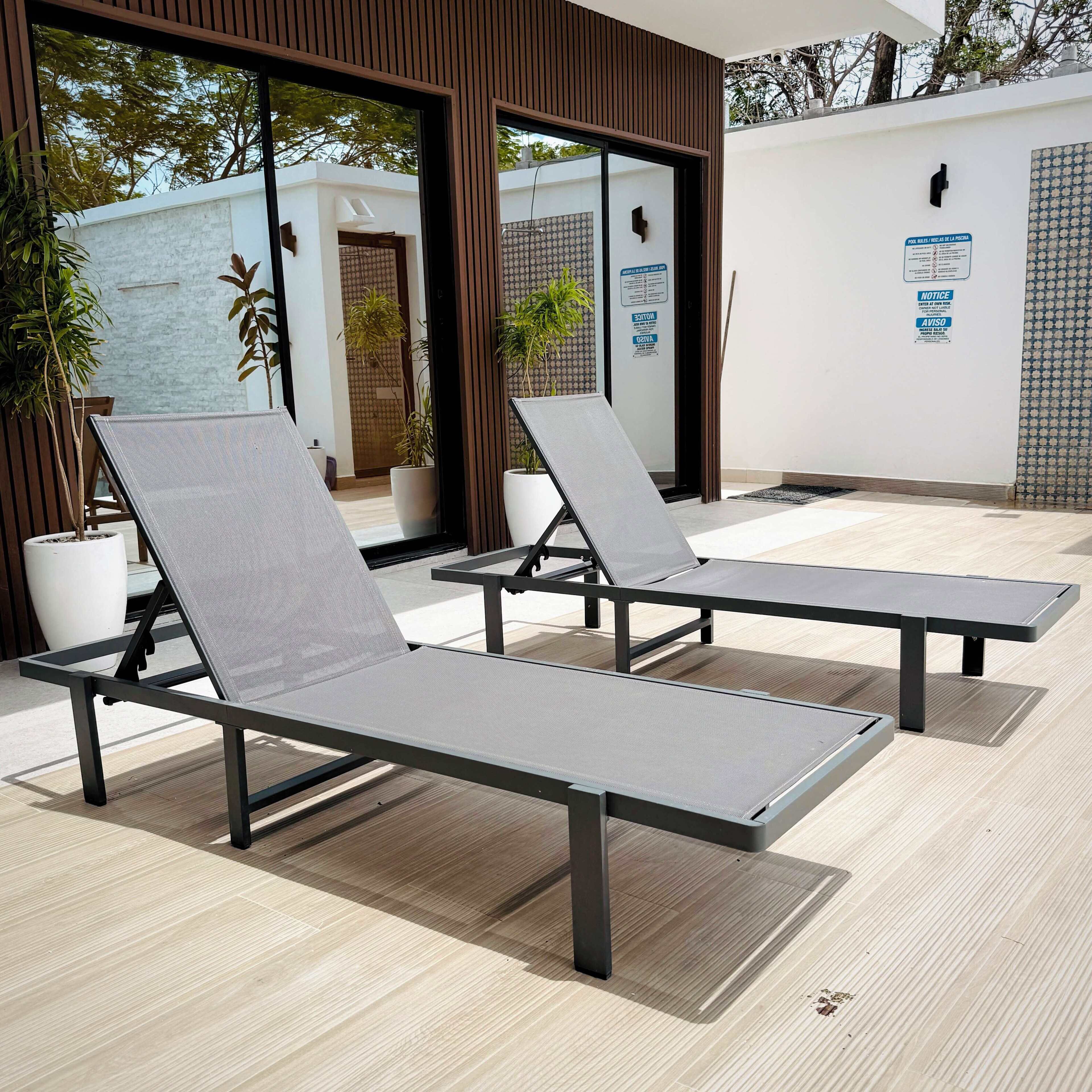 A modern outdoor seating area with two lounge chairs, a potted plant, and a wall with a sign.