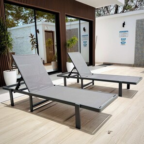 A modern outdoor seating area with two lounge chairs, a potted plant, and a wall with a sign. - Ocean Dream Apartments E1-A1 (San Juan del Sur)
