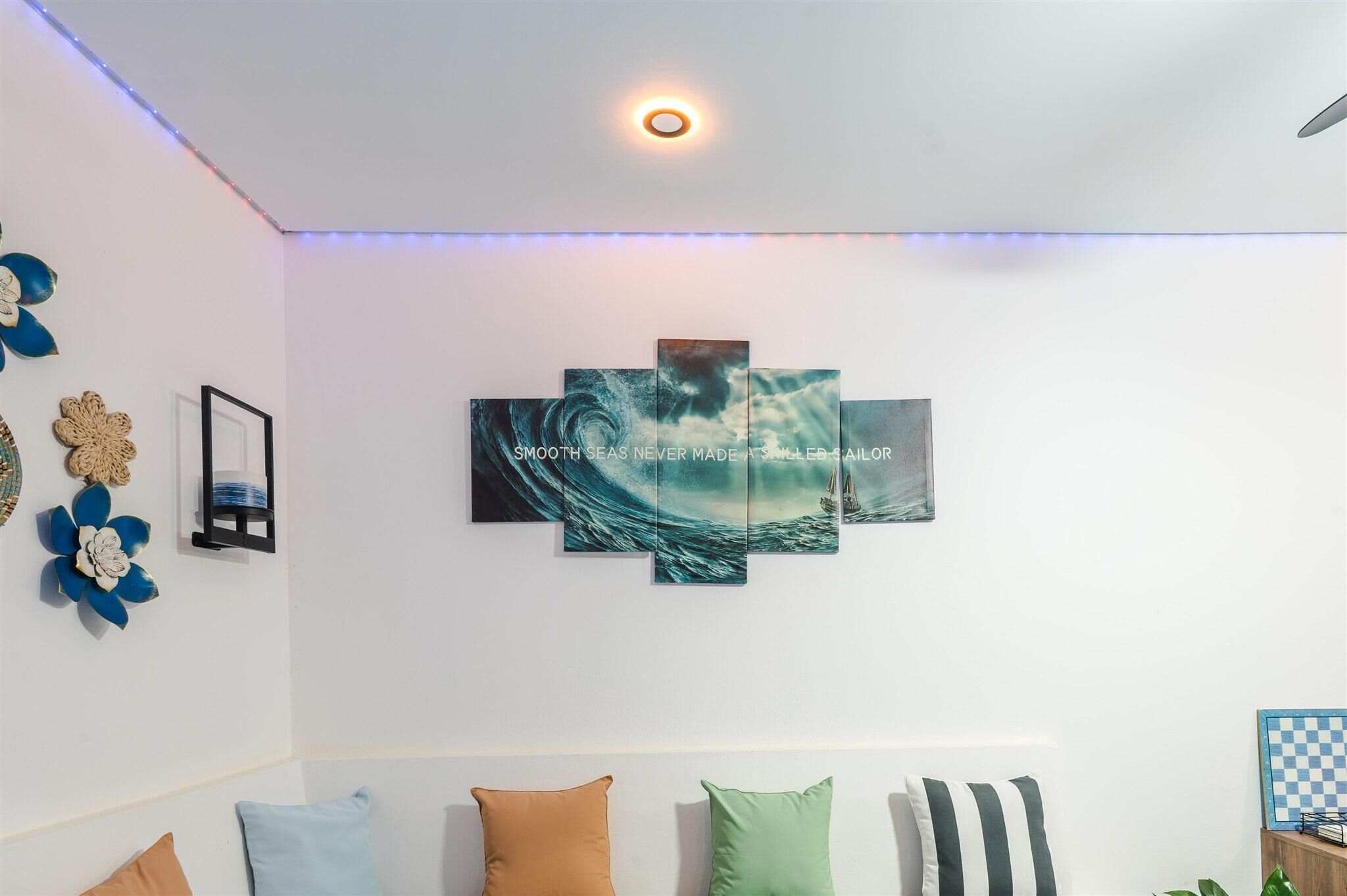 Una habitación con una obra de arte colgada en la pared que representa una escena marina y una lámpara en el techo.