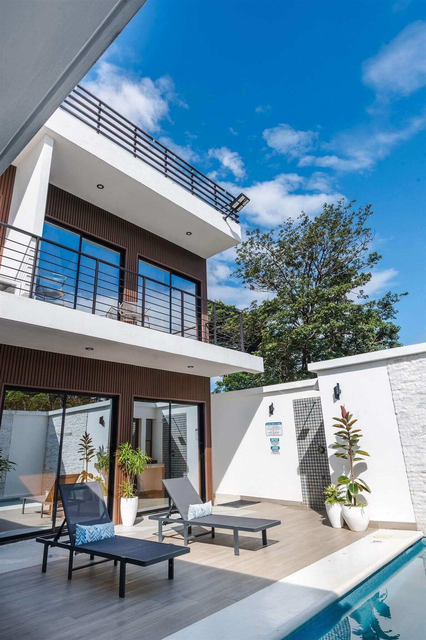 Una moderna casa a due piani con un balcone, una piscina e un'area salotto esterna.