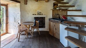 Une cuisine rustique avec une cheminée, des chaises en bois, une table à manger et un réfrigérateur.