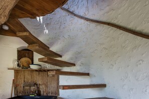 A rustic kitchen with wooden beams, a shelf with dishes, and a kettle.