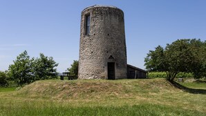 Une tour de pierre dotée d’une porte et d’une fenêtre, entourée d’herbe et d’arbres.