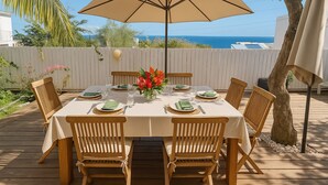 A wooden deck with a table set for six, surrounded by chairs, under a large umbrella. - Close to the beach, house with large swimming pool, ideal for family/friends, sea view. (Saint-Paul)