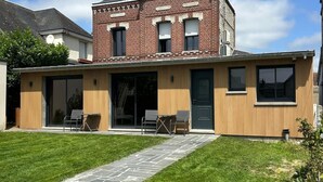 Una casa de dos pisos con fachada de ladrillo, un patio cubierto con área de estar al aire libre y un sendero de piedra que conduce a la entrada.