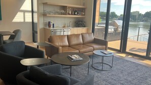 A modern living room with a leather sofa, two armchairs, and a coffee table. A kitchen with a countertop and cabinets is visible in the background. - Lake Minnetonka Retreat (Mound)