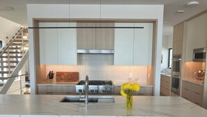 A modern kitchen with a central island, stainless steel appliances, and a vase of yellow flowers. - Lake Minnetonka Retreat (Mound)