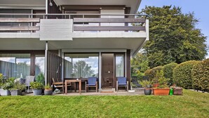 Et moderne hus med to etager, en altan, en terrasse med stole og et bord samt en velplejet græsplæne.