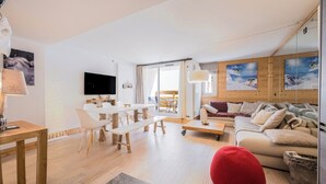 A spacious living area with a large sofa, a dining table with chairs, and a television mounted on the wall. - Renovated apartment for 5 - with balcony (Megève)