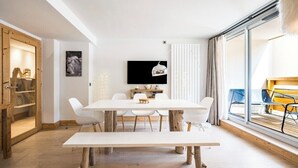 A modern dining area with a white table and chairs, a mounted TV, and a large window with a view of the outdoors. - Renovated apartment for 5 - with balcony (Megève)