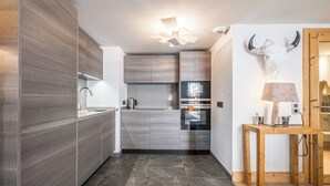 A modern kitchen with grey cabinetry, a stainless steel refrigerator, and a wooden table with a lamp. - Renovated apartment for 5 - with balcony (Megève)