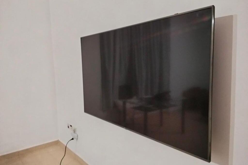 A large flat-screen TV mounted on a white wall in a room with a visible power outlet.