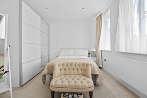 A bedroom with a bed, a chair, a nightstand, and a window with curtains. - London Road Apartment in Isleworth (Isleworth)