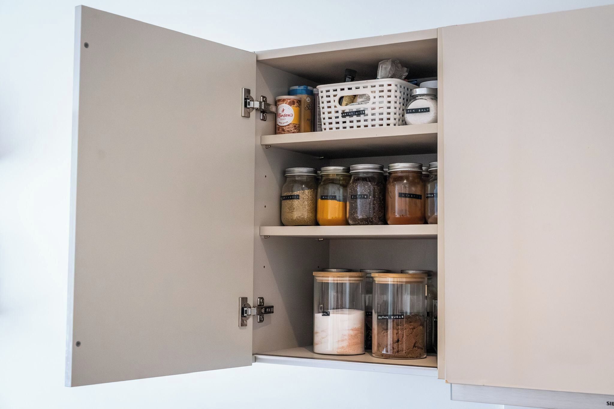 Una despensa con puertas abiertas, que contiene varios recipientes para alimentos y una cesta.