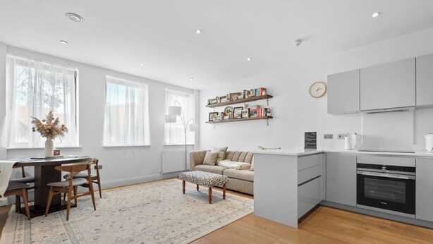 A modern kitchen with grey cabinets, a built-in oven, and a dining area with a wooden table and chairs. - London Road Apartment in Isleworth (Isleworth)