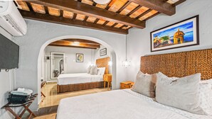 A hotel room with a large bed, a wooden headboard, a painting on the wall, and a TV mounted on the wall. - Old San Juan Pool House & Jacuzzi Grotto (San Juan)