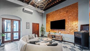 A living room with a large sofa, a coffee table, a flat-screen TV mounted on a textured wall, and a wooden cabinet. - Old San Juan Pool House & Jacuzzi Grotto (San Juan)