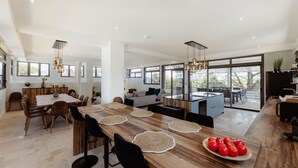 A spacious modern kitchen with a central island, large windows, and a dining area with a wooden table and chairs.