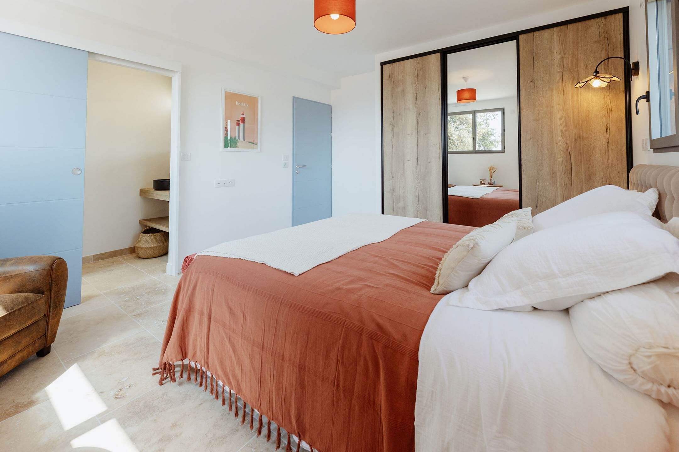 Un dormitorio con cama, un armario de madera, una puerta azul y un baño pequeño con lavabo y espejo.