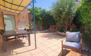 Un patio al aire libre con una mesa y sillas, una silla de madera con cojín y un paraguas amarillo.