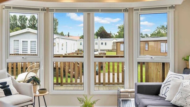 A room with a bay window, a sofa, a small table, and a potted plant. - The Chester-2 bed Static Caravan (Jedburgh)