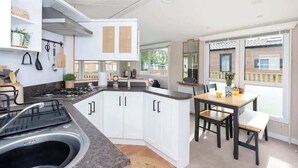 A modern kitchen with white cabinets, a central island, and a dining area with a table and chairs. - The Chester-2 bed Static Caravan (Jedburgh)