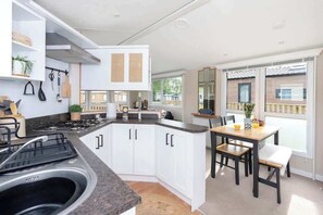 A modern kitchen with white cabinets, a central island, and a dining area with a table and chairs. - The Chester-2 bed Static Caravan (Jedburgh)