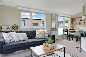 A modern living room with a sofa, coffee table, and dining area. - The Chester-2 bed Static Caravan (Jedburgh)