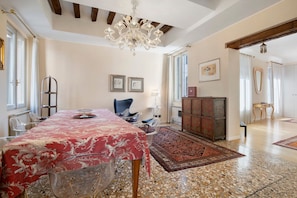 A spacious room with a large dining table, clear chairs, a chandelier, a patterned rug, and a wooden cabinet.