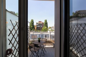 Een balkon met een tafel en stoelen, een bloempot en uitzicht op gebouwen en bomen.