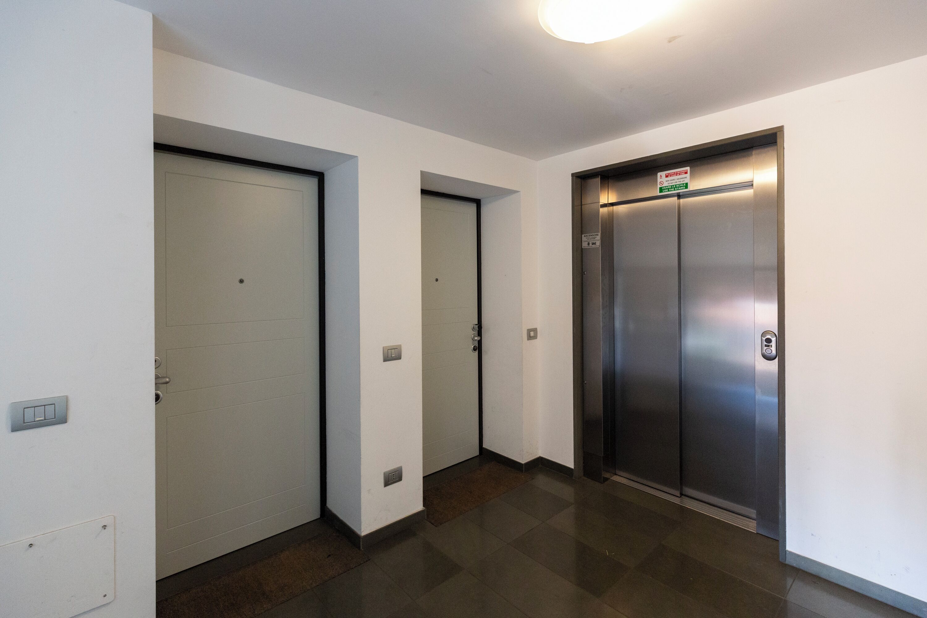 Un pasillo con tres puertas, incluyendo una puerta de ascensor metálica con un letrero encima.