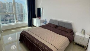 Ein Schlafzimmer mit großem Fenster, einem Bett mit brauner Bettdecke, einem Nachttisch und einem Beistelltisch.
