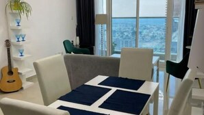 Ein modernes Wohnzimmer mit Essbereich, einer Gitarre und Blick auf die Stadt durch große Fenster.