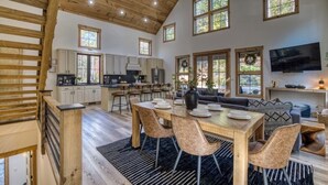 A spacious kitchen with wooden cabinets, a dining area with a table set for four, and a large window overlooking the outdoors. - Luxury Blue Ridge Cabin • Hot Tub • Sauna • Game Room • 2 Private Acres (Blue Ridge)