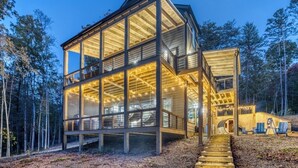 A modern wooden cabin with large glass windows and a wooden deck, surrounded by trees. - Luxury Blue Ridge Cabin • Hot Tub • Sauna • Game Room • 2 Private Acres (Blue Ridge)