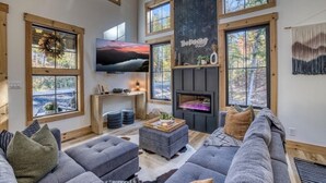 A spacious living room with a fireplace, large windows, a flat-screen TV, and a cozy seating area. - Luxury Blue Ridge Cabin • Hot Tub • Sauna • Game Room • 2 Private Acres (Blue Ridge)