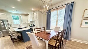 Una cocina moderna con armarios blancos, una mesa de comedor de madera y una pared azul de acento.
