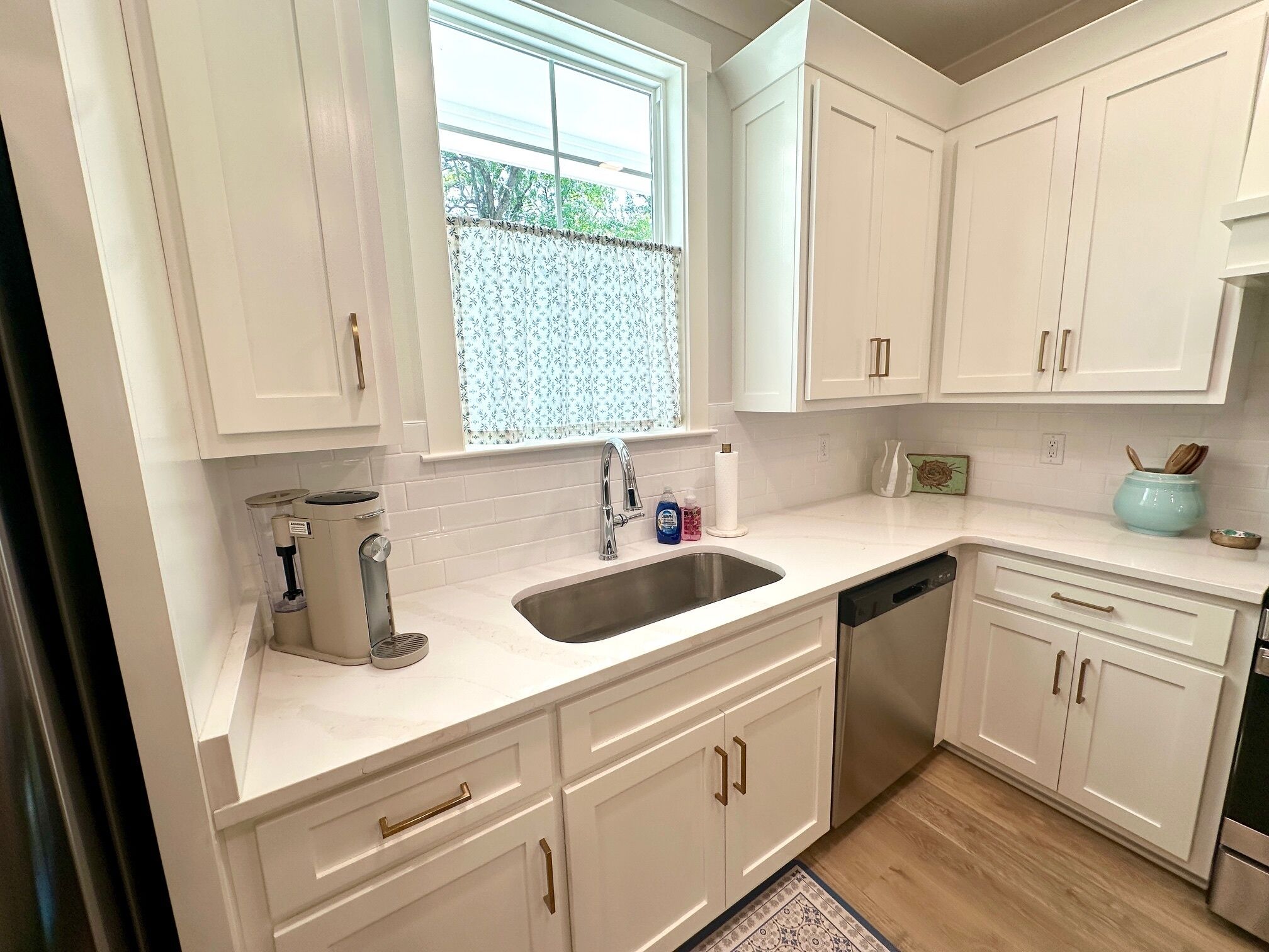 A modern kitchen with white cabinets, a stainless steel sink, and a built-in dishwasher.