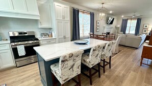 Una cocina moderna con armarios blancos, una estufa de acero inoxidable y una isla grande con taburetes de bar.